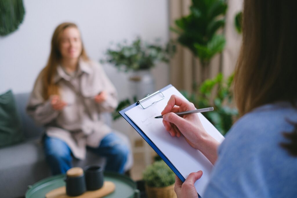 pexels-photo-7176026-7176026 Unrecognizable professional female psychologist writing on clipboard while sitting against client on blurred background during psychotherapy session in light office
